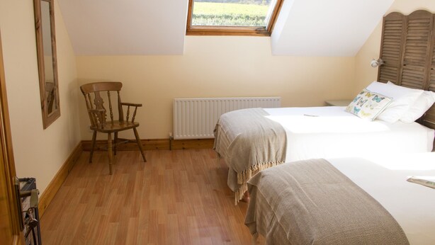 A bedroom with two beds, a wooden chair, a radiator, and a window with a view of the outdoors. - Madra Rua Organic Accommodation (Ballyliffin)