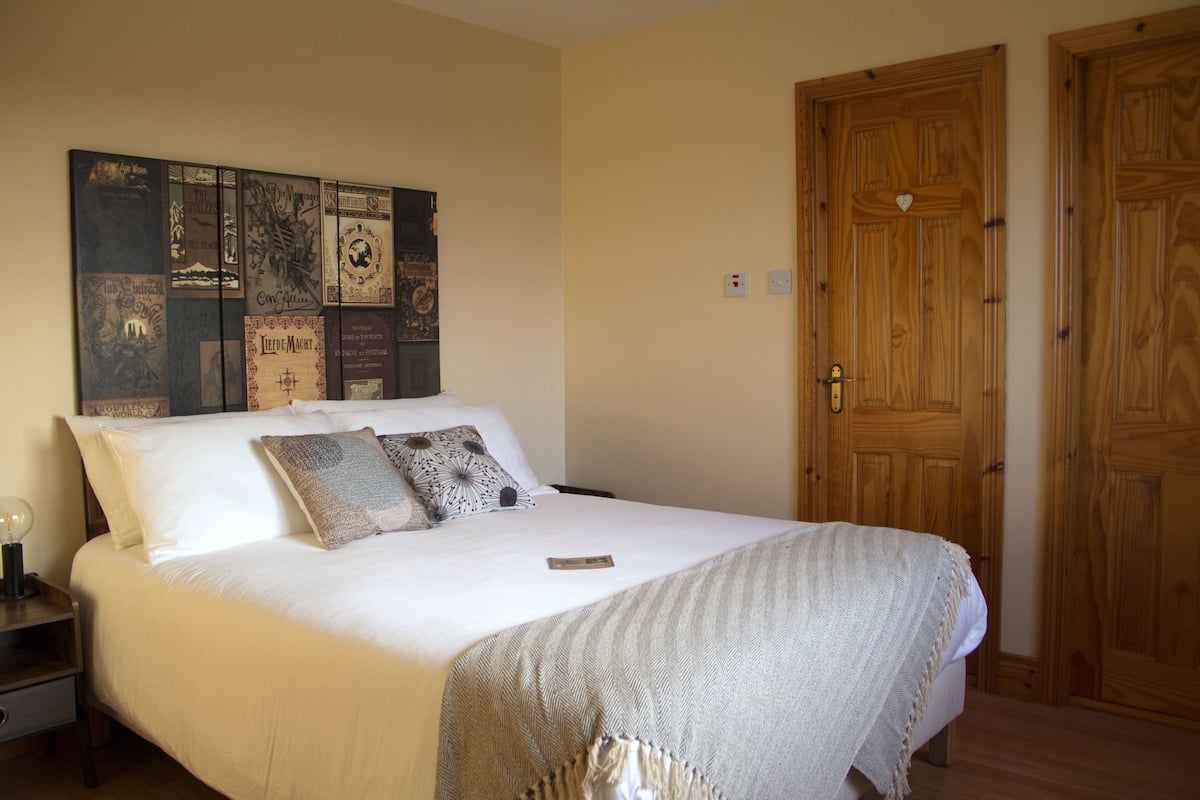 A neatly made bed with a patterned throw, a wall with various framed pictures, and a wooden door.