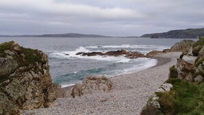 Una playa rocosa con olas rompiendo en la orilla, rodeada de acantilados.