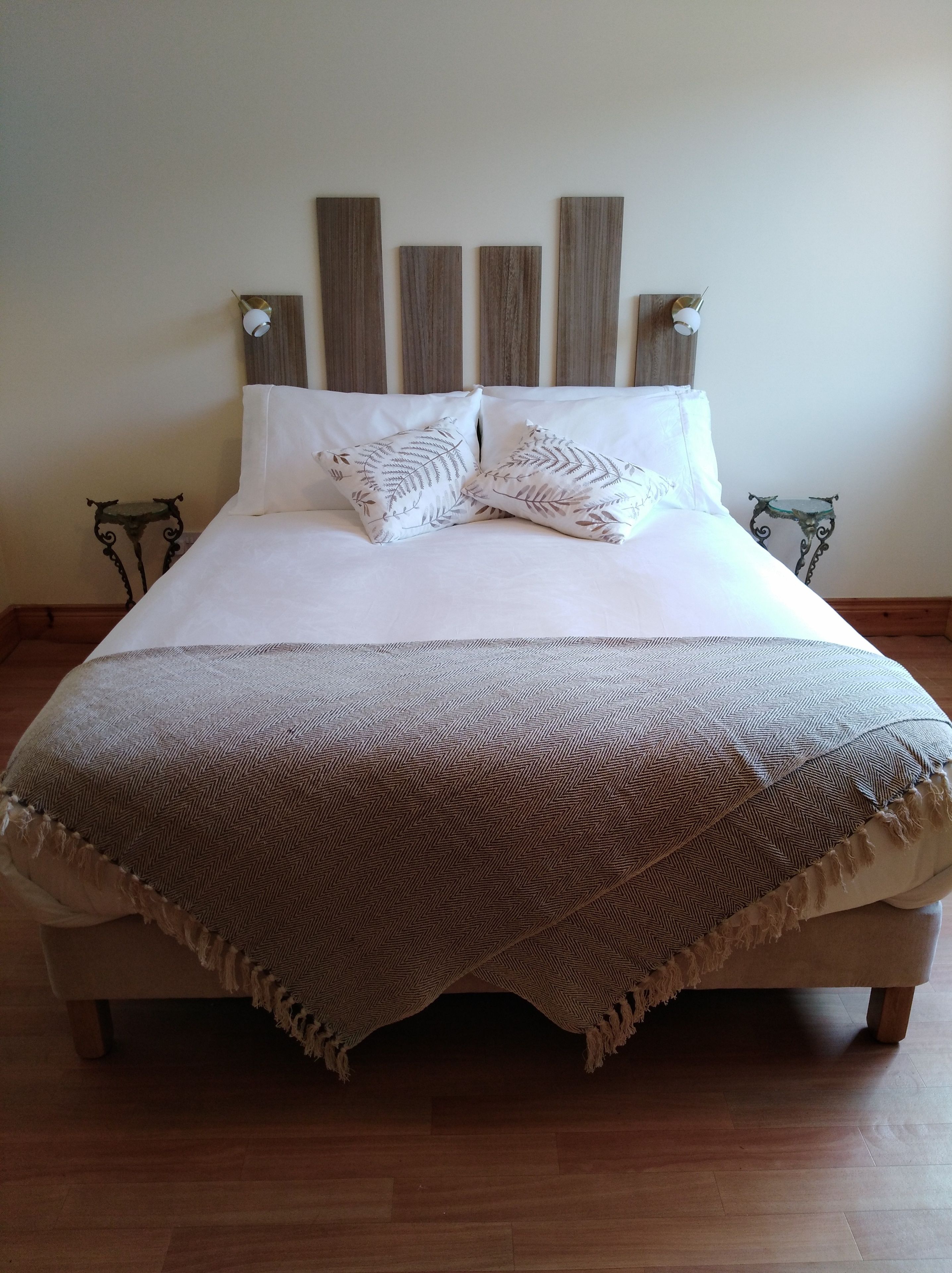 A bed with a wooden headboard, white bedding, and a patterned throw blanket.