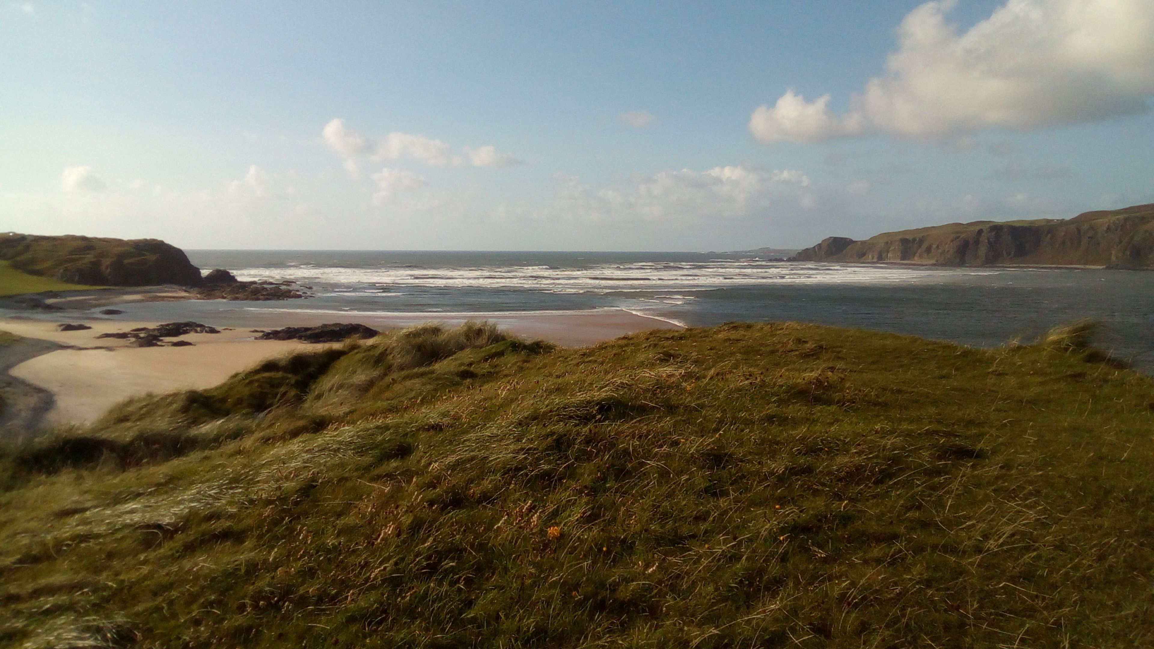 Een kustlandschap met een zandstrand, groene heuvels en de oceaan.
