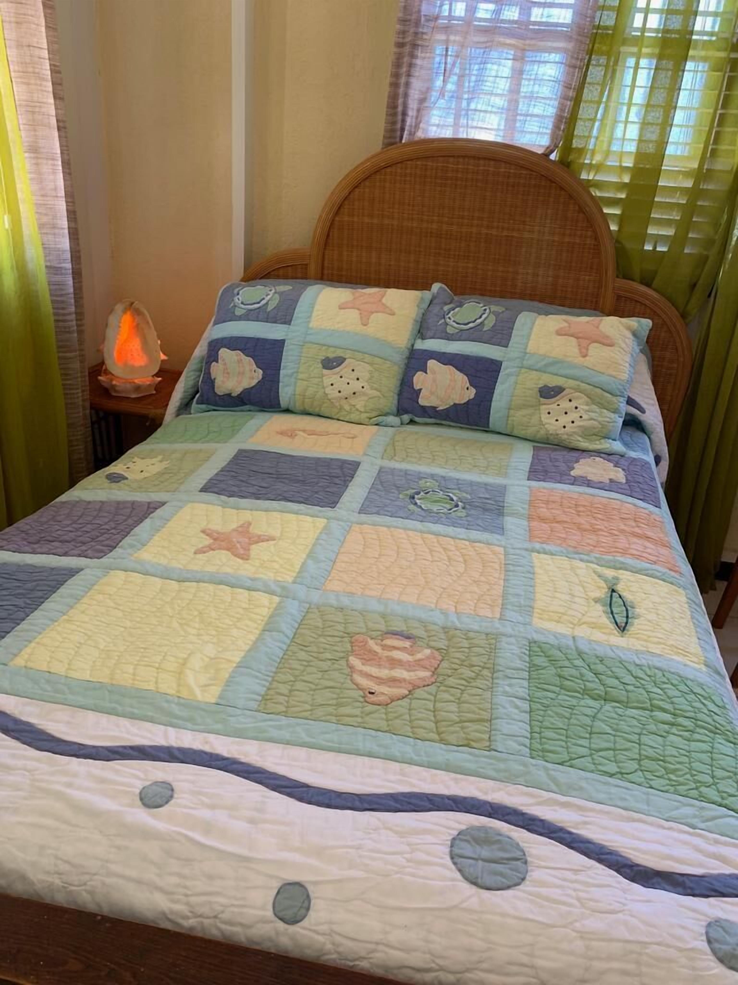 Una cama con colcha temática náutica, cabecera de mimbre y lámpara de noche.