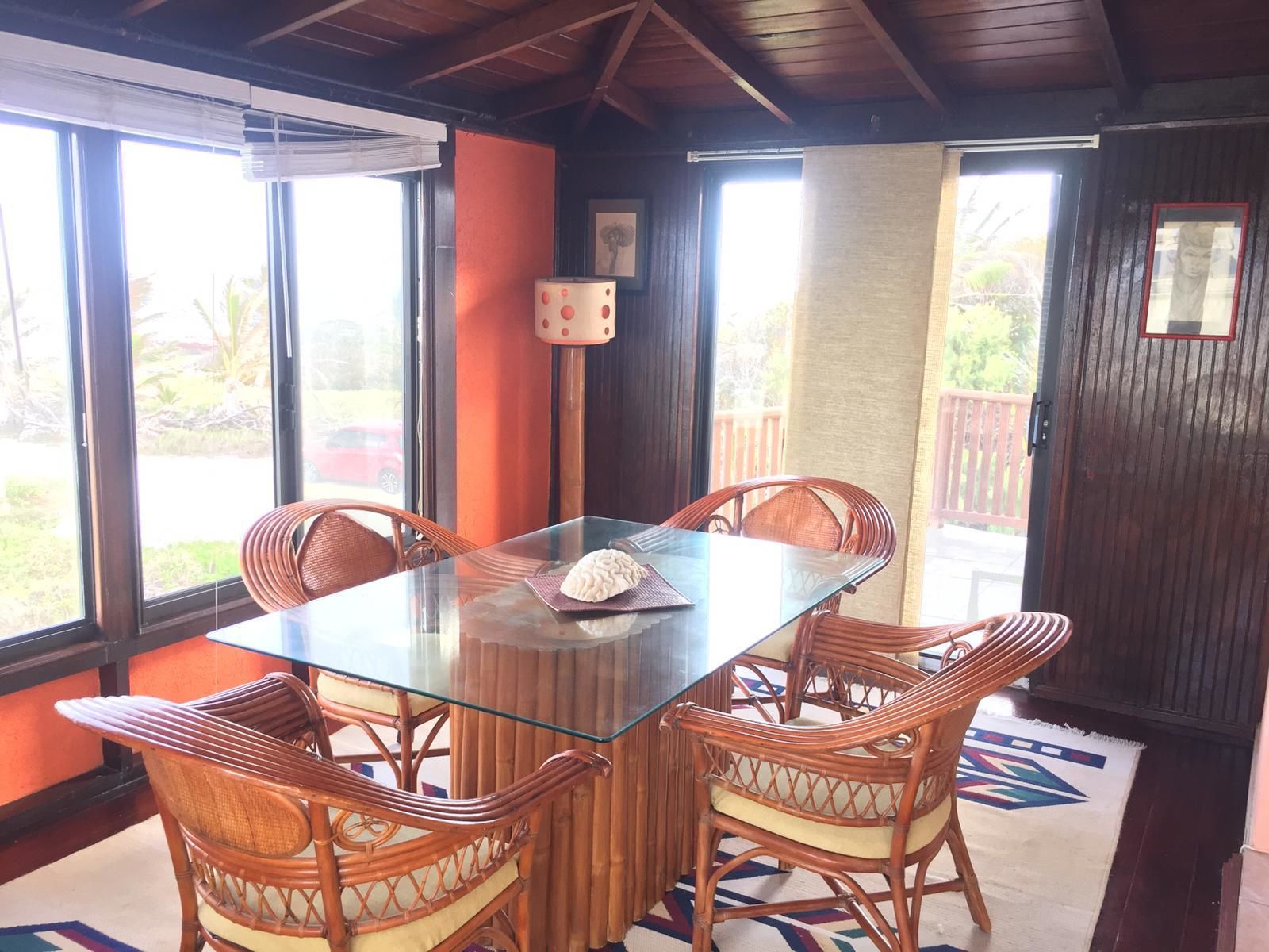 A dining area with a glass table and wicker chairs, large windows, and a view of the outdoors.