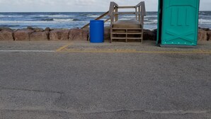 Une plage avec un banc en bois, un baril bleu et des toilettes portables.