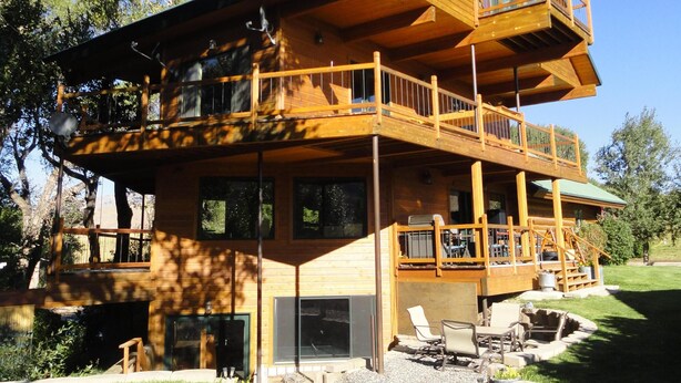 Une cabane en bois à deux étages, dotée d’un balcon, de grandes fenêtres et d’une pelouse bien entretenue.