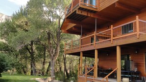 Une cabane en bois à deux étages, dotée d’un balcon, entourée d’une pelouse bien entretenue et d’arbres.
