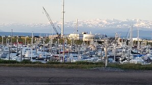 A marina with numerous boats docked, a crane, and a building in the background with snow-capped mountains.