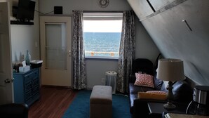 A room with a view of the sea, a sofa, a lamp, a small table, and a cabinet.