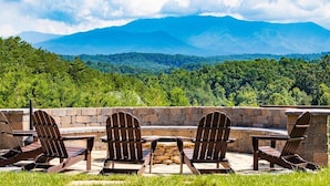 Eine Terrasse mit Adirondack-Stühlen und einem Steintisch, mit Blick auf ein bewaldetes Gebirge.