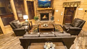 Ein gemütliches Wohnzimmer mit Kamin aus Stein, Ledersofas und einem darüber montierten Fernseher.
