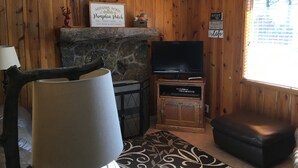 Een gezellige woonkamer met houten wanden, een stenen open haard, een flatscreen televisie en een comfortabele zithoek.