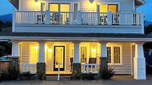 A two-story house with a balcony on the upper floor and a covered front porch on the lower floor. - Two King Suites, Ocean Views & Upscale Touches in Downtown Manzanita (Manzanita)