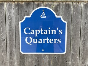 Een blauw bord met de tekst 'Captain's Quarters' op een houten achtergrond.