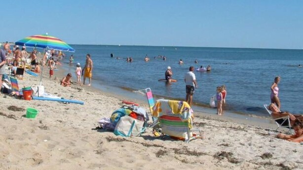 Een strand met mensen die zwemmen en zonnebaden, parasols en strandstoelen.