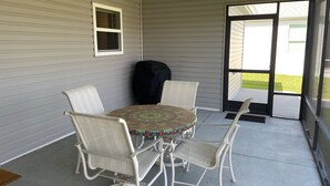Eine überdachte Terrasse mit Tisch und vier Stühlen, einem Deckenventilator und einer Schiebetür.