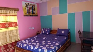 A bedroom with a bed, a nightstand, a table, and a chair. - Orchidée Hôtel (Kpalimé)