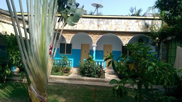 A courtyard with a stone building featuring blue and beige walls, arched doorways, and a satellite dish. - Orchidée Hôtel (Kpalimé)