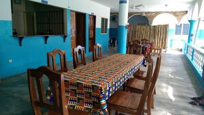 A dining area with a long table covered with a colorful tablecloth, surrounded by wooden chairs. - Orchidée Hôtel (Kpalimé)