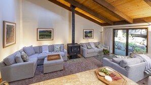 A cozy living room with two grey sofas, a wooden ceiling, and a large window with a view of greenery. - Wine Country Redwood Estate in the Heart of Wine Country (Santa Rosa)