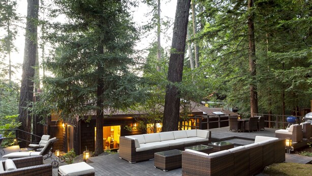 An outdoor deck with wicker furniture and a built-in seating area surrounded by tall trees. - Wine Country Redwood Estate in the Heart of Wine Country (Santa Rosa)