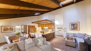 A spacious living area with a wooden ceiling, a dining table with chairs, a sofa with cushions, a kitchen area with wooden cabinets, and a fireplace. - Wine Country Redwood Estate in the Heart of Wine Country (Santa Rosa)
