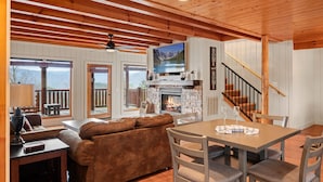 A cozy living room with a fireplace, a TV mounted above it, and a wooden ceiling.