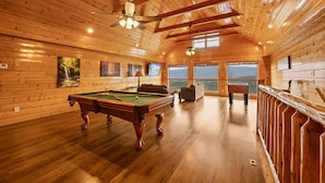 A spacious room with a pool table, comfortable seating, and large windows offering a view of the outdoors.