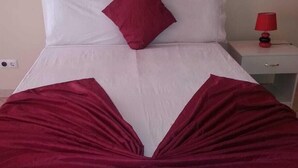 A bed with a white and red bedspread, a red pillow, and a red lamp on a bedside table. - Casa anilda & albino (São Filipe)
