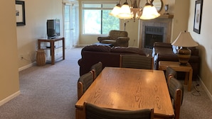 Una sala de estar con una mesa de comedor de madera, sillas, un sofá, una chimenea y un televisor sobre un mueble.
