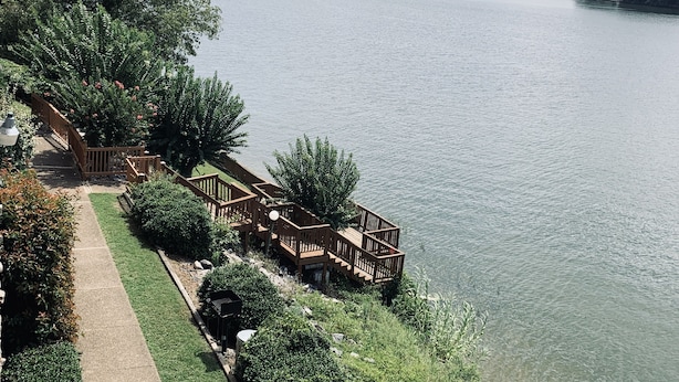Una propiedad junto al lago con una terraza de madera con vistas al agua, un sendero y abundante vegetación.