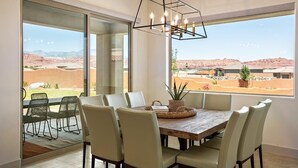 A dining area with a wooden table and chairs, a hanging light fixture, and large windows offering a view of a desert landscape. - Arcadia 30 | PAC-MAN * Asteroids Arcade * Games * Balcony Views * Resort Ameniti (Santa Clara)
