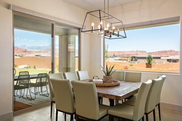 A dining area with a wooden table and chairs, a hanging light fixture, and large windows offering a view of a desert landscape. - Arcadia 30 | PAC-MAN * Asteroids Arcade * Games * Balcony Views * Resort Ameniti (Santa Clara)