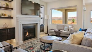 A modern living room with a fireplace, a flat-screen TV, a sofa, and a large window offering a view of the desert. - Arcadia 30 | PAC-MAN * Asteroids Arcade * Games * Balcony Views * Resort Ameniti (Santa Clara)