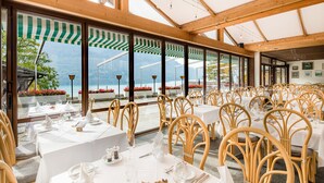 En restaurant med flere spiseborde, store vinduer med udsigt til bjerge og trælofter.