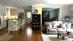A spacious living room with a sofa, coffee table, and a dining area with chairs and a chandelier. - Home with lots of space for everyone on a quiet street in 5 points with pool! (Athens)