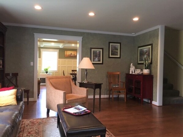 A living room with a brown leather sofa, a brown armchair, a wooden coffee table, and a red bench. There are framed pictures on the wall and a lamp on a side table. - Spacious Talkeetna home on Ruth Glacier Avenue (Talkeetna)