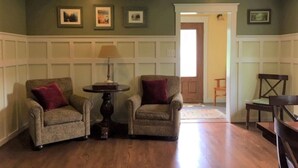 A room with two armchairs, a small table with a lamp, wooden flooring, and framed pictures on the wall. - Spacious Talkeetna home on Ruth Glacier Avenue (Talkeetna)
