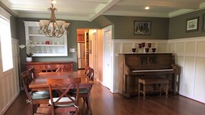 A spacious dining area with a wooden table and chairs, a chandelier, and a piano. - Spacious Talkeetna home on Ruth Glacier Avenue (Talkeetna)