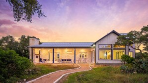 Une maison moderne avec une façade en pierre, un patio couvert et un chemin menant à l’entrée.