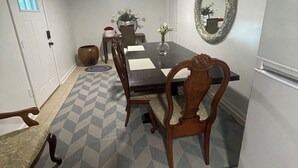 Un comedor con una mesa rectangular, seis sillas de madera, un tapete estampado, una puerta blanca y un espejo fijado a la pared.
