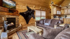 A cozy log cabin interior with a stone fireplace, leather furniture, and a mounted fur. - Appalachian Adventure - 4 Bedroom sleeps 14! (Gatlinburg)