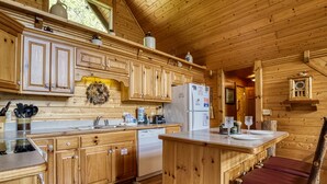 A wooden cabin kitchen with wooden cabinets, a refrigerator, a sink, and a dining area with a table and chairs. - Appalachian Adventure - 4 Bedroom sleeps 14! (Gatlinburg)