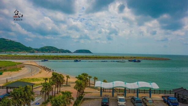 A coastal parking area with cars, a beach, and boats in the distance. - Taijing Hotel (Beigan)