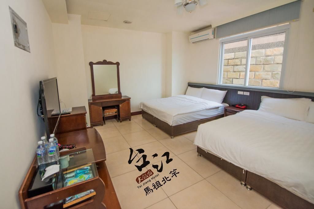 A hotel room with two beds, a desk, a mirror, and a window.
