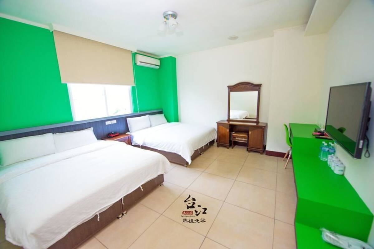 A hotel room with two beds, a TV, a desk, and a green counter.