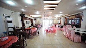 A dining area with round tables and chairs, a kitchen area with appliances, and a large window providing natural light. - Taijing Hotel (Beigan)