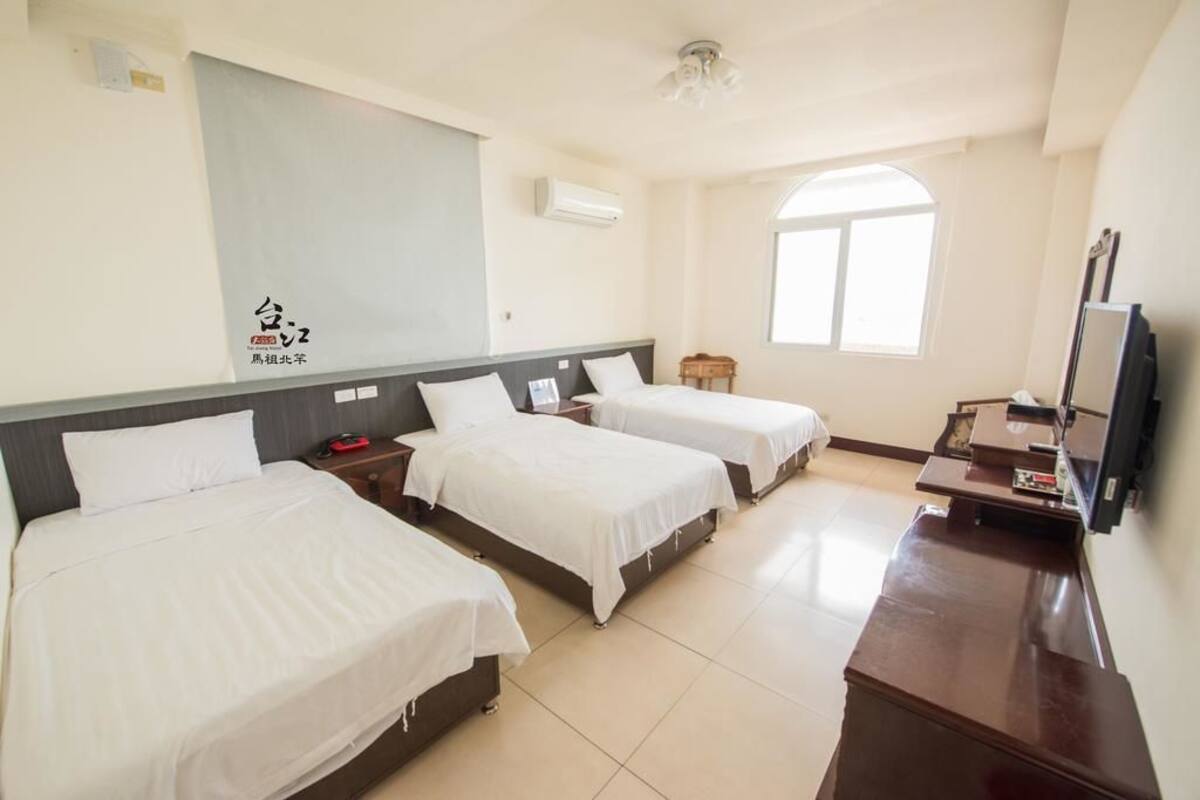 A hotel room with two beds, a desk, a TV, and a large window.