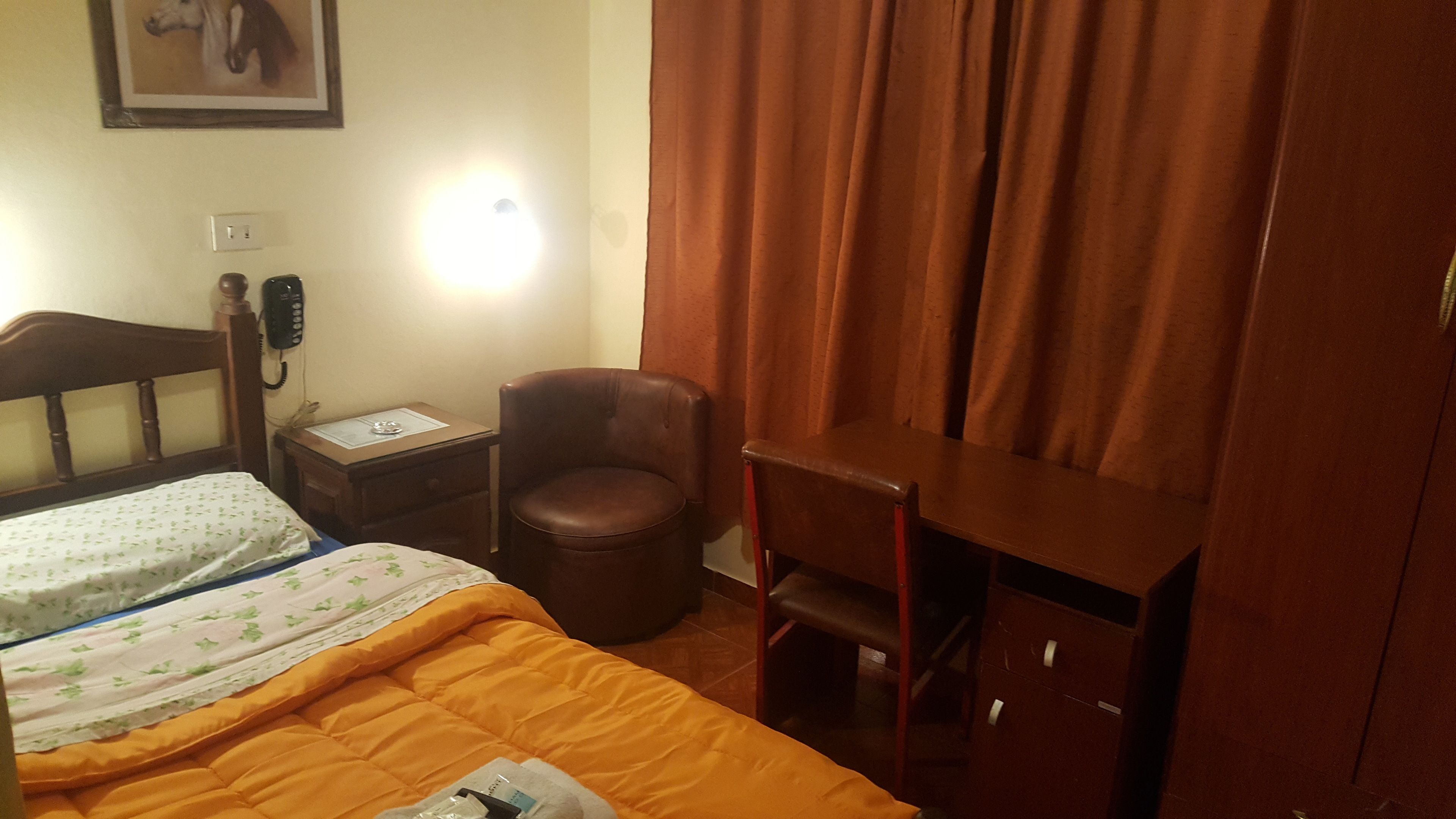 Habitación de hotel con cama, escritorio, silla, mesita de noche y teléfono en la pared.