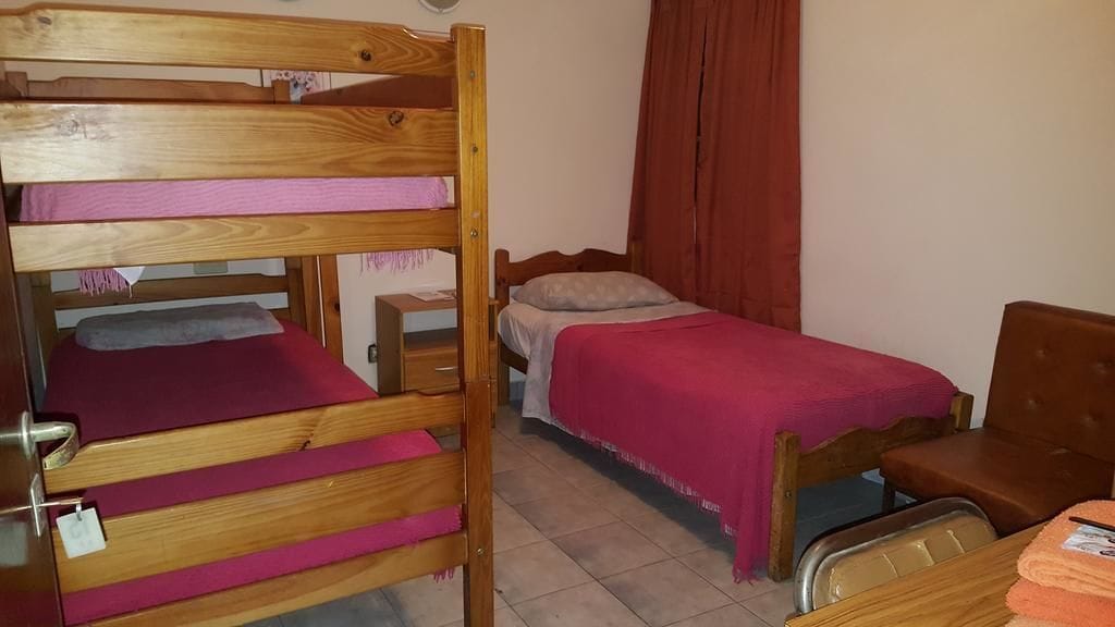 A dormitory room with bunk beds, a single bed, a desk, and a chair.