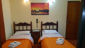 A hotel room with two beds, an orange bedspread, a painting of a sunset, a phone on the nightstand, and a door with a number. - Hotel Paris (General San Martin)